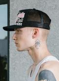 Man wearing Pieces Big Cat mesh Trucker Hat Black Pink close up view from the shoulders up, side profile view Pieces Big Cat Trucker Hat Black Pink - Image 5 | Authenticated at Pieces Los Angeles