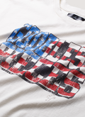 Pieces No Vacancy GBP Rhinestone Tee Shirt Off White garment dyed with screen printed logo of the American flag, cut and sewn garment, boxy cropped fit, handset cross rhinestone pattern, hand distressed details, close up view of the graphic that says God Bless Pieces Pieces GBP Rhinestone Tee Off White - Image 3 | Authenticated at Pieces Los Angeles