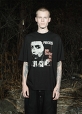 Person outside in the dark wearing the Pieces Inhumane Tee Vintage Black shirt facing the camera Pieces Inhumane Tee Vintage Black - Image 4 | Authenticated at Pieces Los Angeles