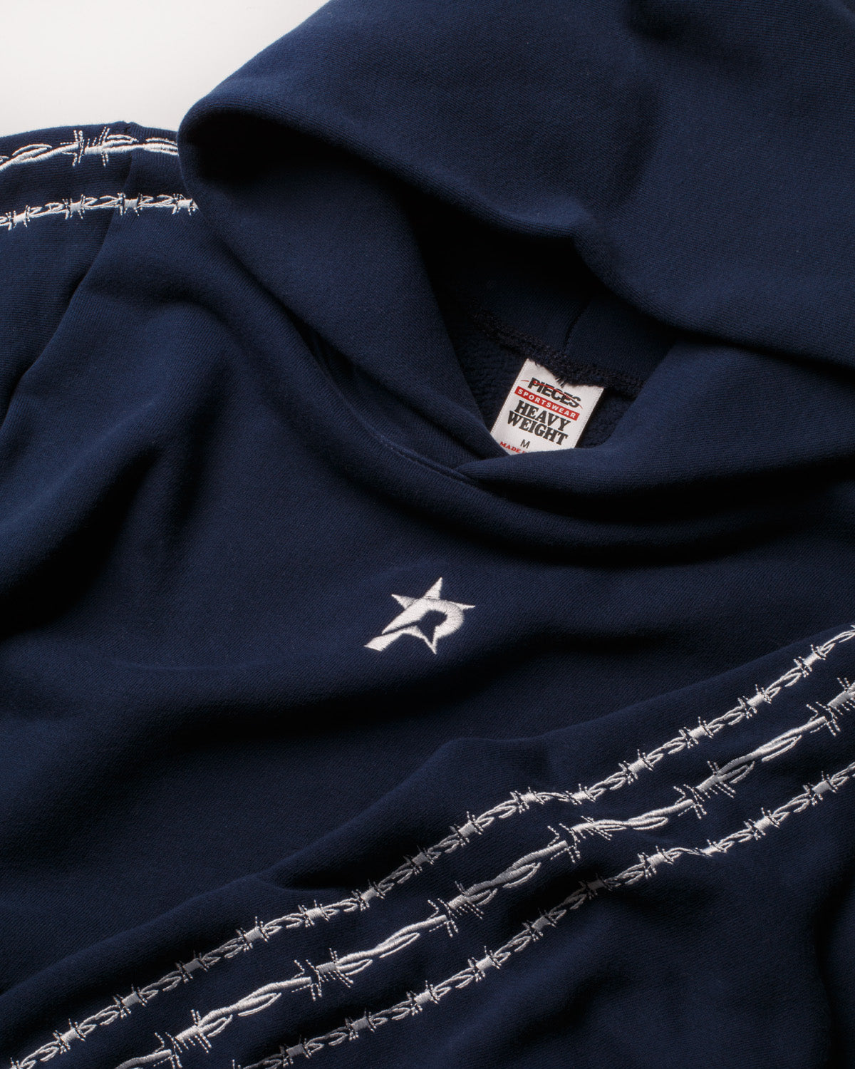 Pieces Wired Sweatshirt Navy Blue close up view of neck with tag, hood, and P star logo on the front, sleeves with barbed wires on them