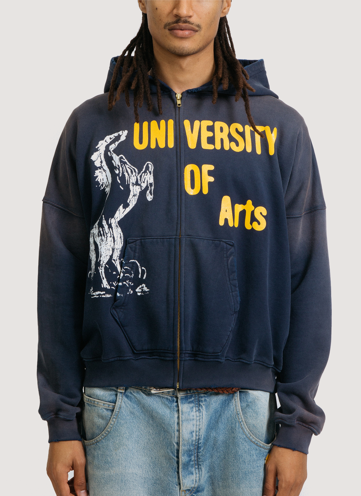 on-body shot of a man wearing the Pieces Academia Zippered Sweatshirt hoodie Vintage Navy blue  with yellow text that says University of Arts and a logo of a horse