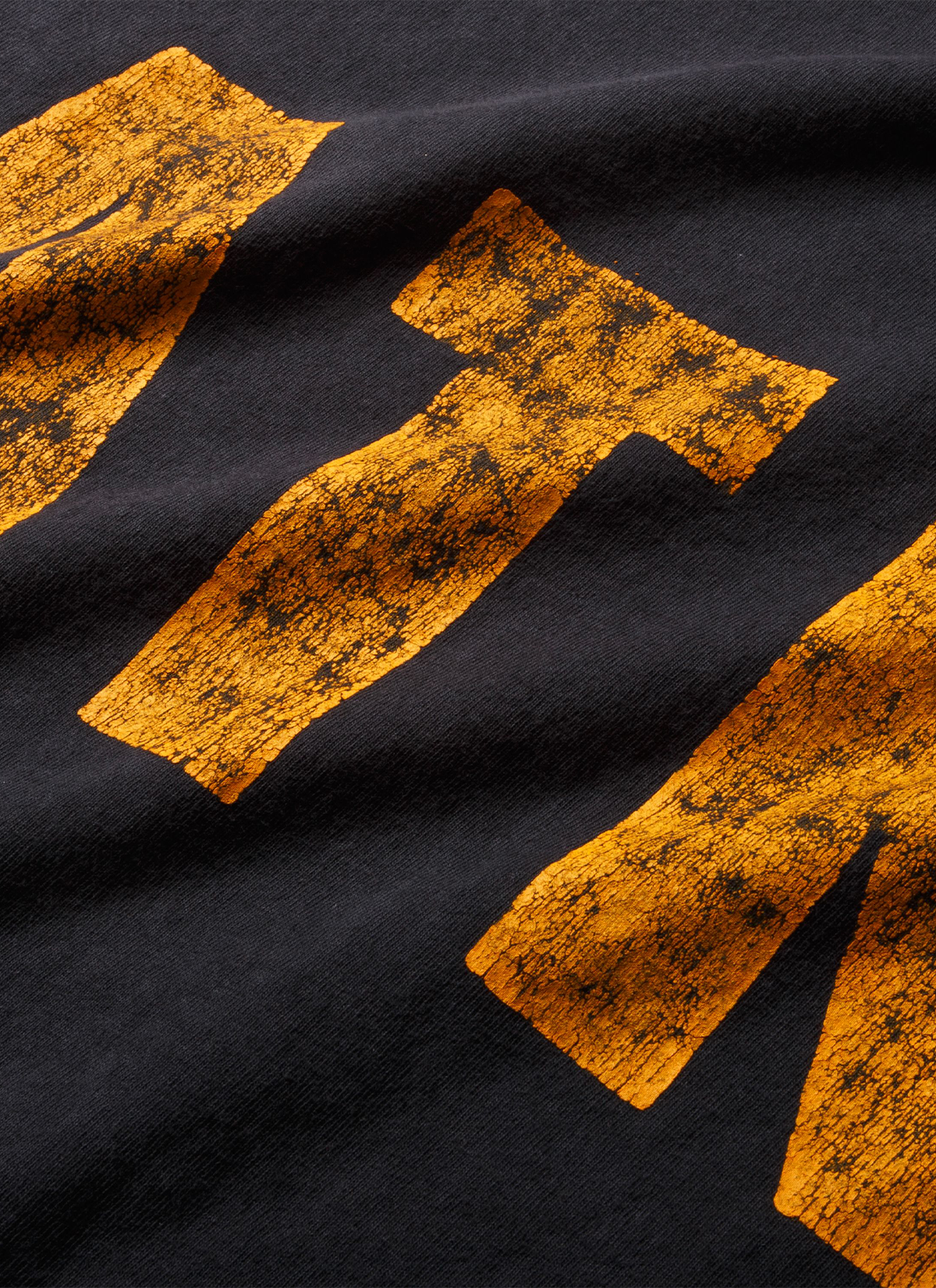 Gallery Dept Distressed ATK Tee Shirt Washed Black close up view of the vintage gold yellow text on the front side Gallery Dept. Distressed ATK Tee Washed Black - Image 4 | Authenticated at Pieces Los Angeles