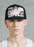 Man wearing Pieces Big Cat mesh Trucker Hat Black Pink that says Big Cats Are Dangerous But A Little Pussy Never Hurt Nobody!, close up view from the shoulders up, facing the camera Pieces Big Cat Trucker Hat Black Pink - Image 4 | Authenticated at Pieces Los Angeles