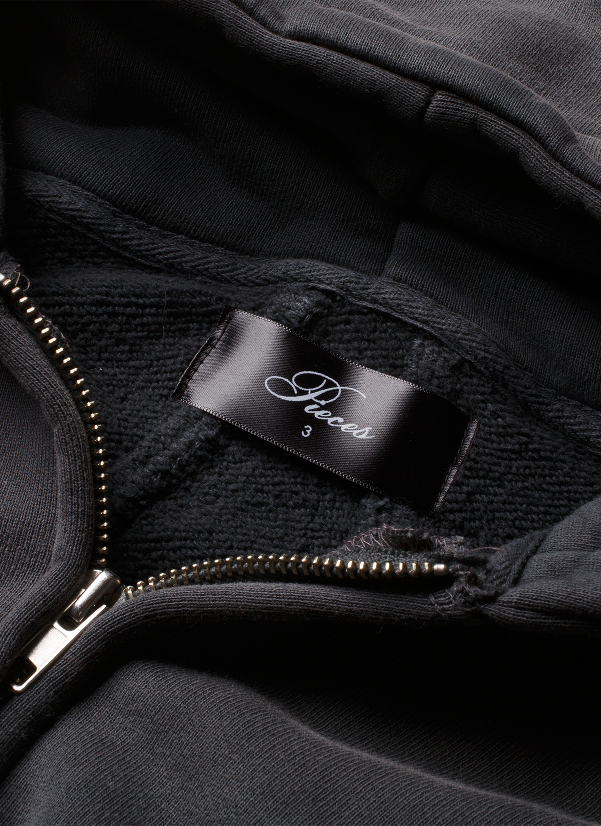 Close up of the tag on the Pieces Basic Program Zip Up Sweatshirt Washed Black grey hoodie with zipper partially opened Pieces Basic Program Zip Up Sweatshirt Washed Black - Image 5 | Authenticated at Pieces Los Angeles