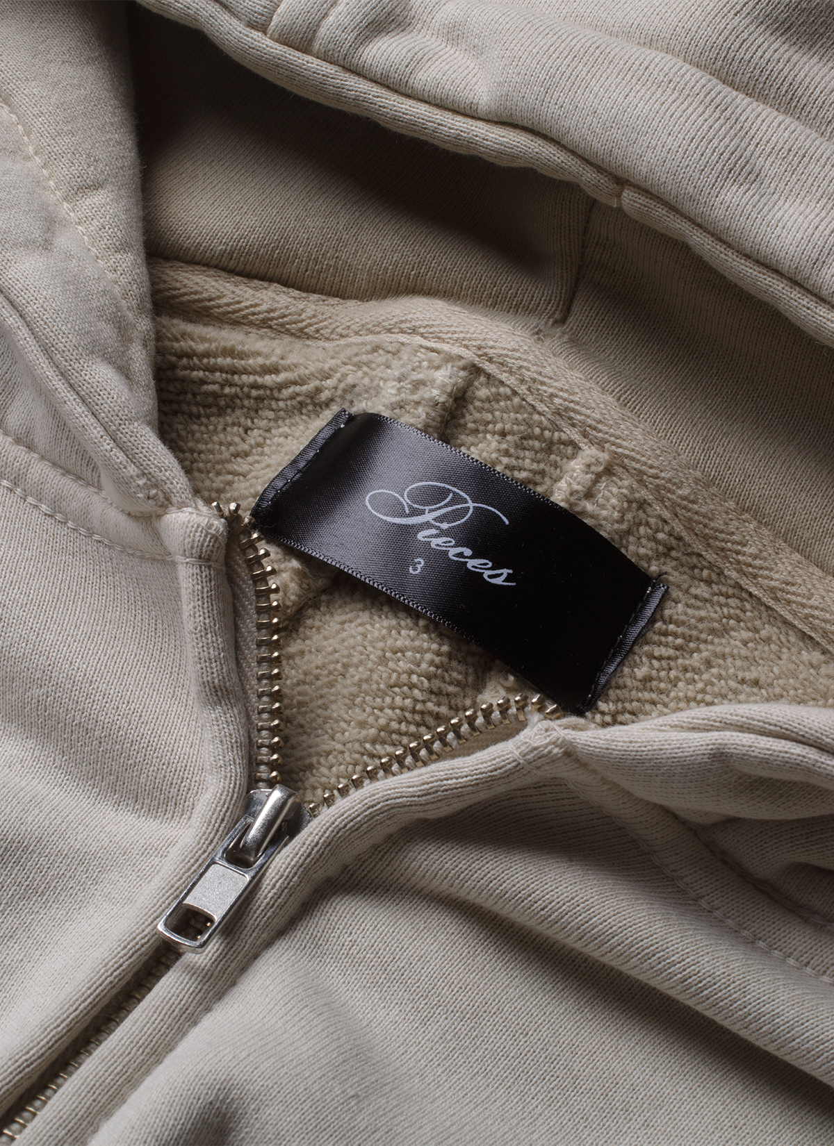 Pieces Basic Program Zip Up Sweatshirt Bone White Off-White close up view of the neck tag and zipper Pieces Basic Program Zip Up Sweatshirt Bone - Image 5 | Authenticated at Pieces Los Angeles