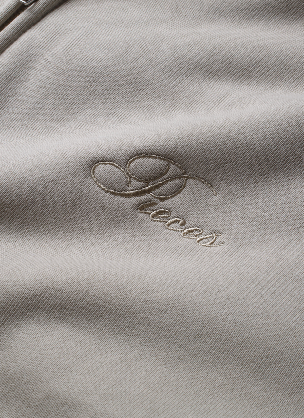 Pieces Basic Program Zip Up Sweatshirt Bone White Off-White front view close up of cursive Pieces logo Pieces Basic Program Zip Up Sweatshirt Bone - Image 6 | Authenticated at Pieces Los Angeles