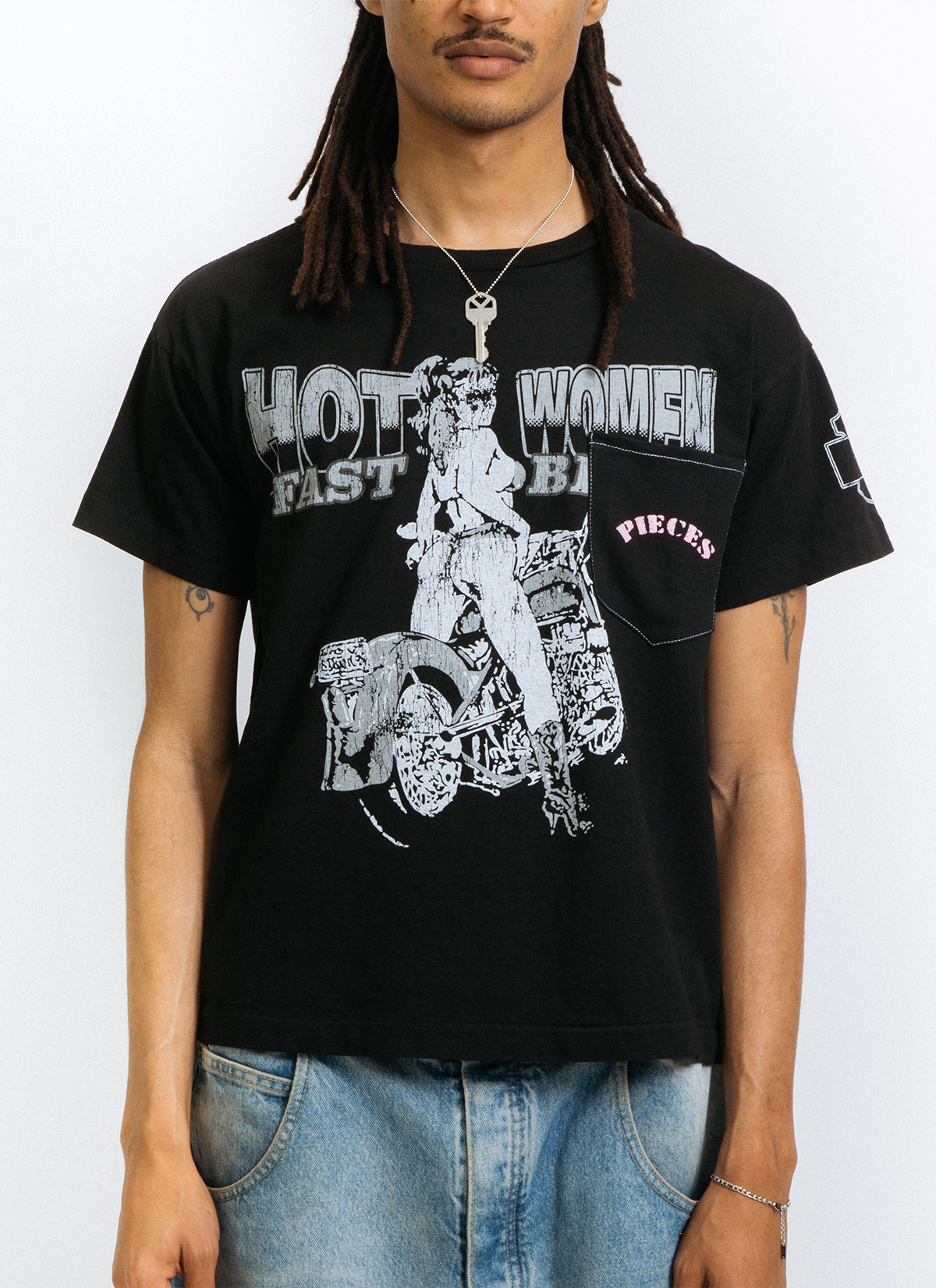 Man wearing the Pieces Fast Bikes Pocket Tee Shirt Vintage Black with graphic of woman riding a motorcycle, with a front pocket with pink text on it, front view