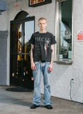 man standing in front of store facing the camera wearing the Pieces F***ed vintage black tee shirt with paint splatter on the shirt with vintage text and graphics Pieces F***ed Tee Vintage Black - Image 5 | Authenticated at Pieces Los Angeles