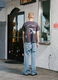 man standing in front of store facing away from the camera wearing the Pieces Future Tee shirt Vintage Black with blue jeans Pieces Future Tee Vintage Black - Image 6 | Authenticated at Pieces Los Angeles