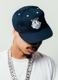 Photo of man wearing a chain and the Pieces God Vs Devil Baseball Cap Navy Blue with a graphic of a Native American Indian head with a halo Pieces God Vs Devil Baseball Cap Navy - Image 6 | Authenticated at Pieces Los Angeles