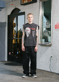 man standing in front of a ticket booth wearing the Pieces Influence Cut Off Vintage faded Black tank top facing the camera Pieces Influence Cut Off Vintage Black - Image 5 | Authenticated at Pieces Los Angeles