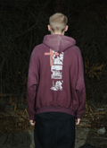 Man standing in the forest at night facing away, wearing the Pieces Inhumane Half Zip Sweatshirt Vintage Maroon hoodie with half-zip zipper, graphics and text on the hoodie Pieces Inhumane Half Zip Sweatshirt Vintage Maroon - Image 5 | Authenticated at Pieces Los Angeles