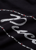Pieces Jeweled Sweatshirt Black Hoodie with a cursive Pieces logo surrounded by red rhinestone jewels front view, close up Pieces Jeweled Sweatshirt Black - Image 5 | Authenticated at Pieces Los Angeles