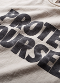 Gallery Dept. Protect Your Neck Tee Vintage White with faded black text, close up view of front Gallery Dept. Protect Your Neck Tee Vintage White - Image 3 | Authenticated at Pieces Los Angeles