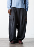 Man wearing the Pieces Repair Pleated Sweatpants Vintage Black with Japanese style repair stitch work, front view, with loafers and a blue long sleeve shirt and white background Pieces Repair Pleated Sweatpants Vintage Black - Image 6 | Authenticated at Pieces Los Angeles