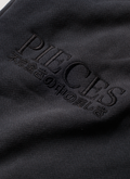 Pieces Repair Pleated Sweatpants Vintage Black close up view of Pieces text and japanese text underneath Pieces Repair Pleated Sweatpants Vintage Black - Image 5 | Authenticated at Pieces Los Angeles